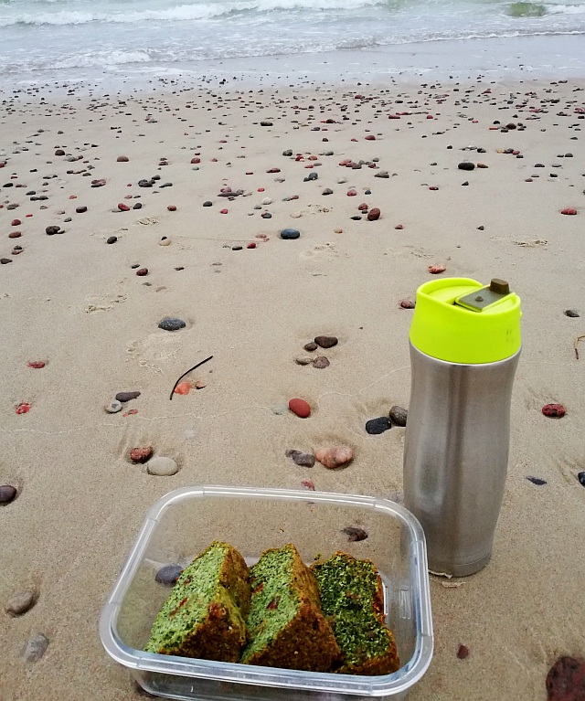 Termosinis puodelis ir indas su pyragu ant jūros kranto